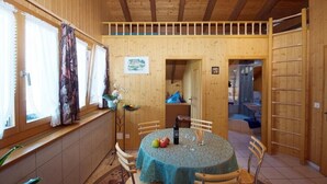 A wooden interior with a dining table, chairs, and a window with curtains. - Chalet Häsi 3 (4) room attic apartment (Hasliberg-Wasserwendi)