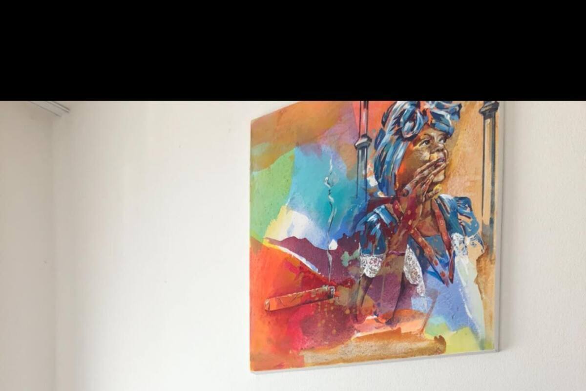 Un letto con lenzuola bianche e cuscini rossi, un cane sdraiato sopra e un quadro astratto colorato appeso al muro.