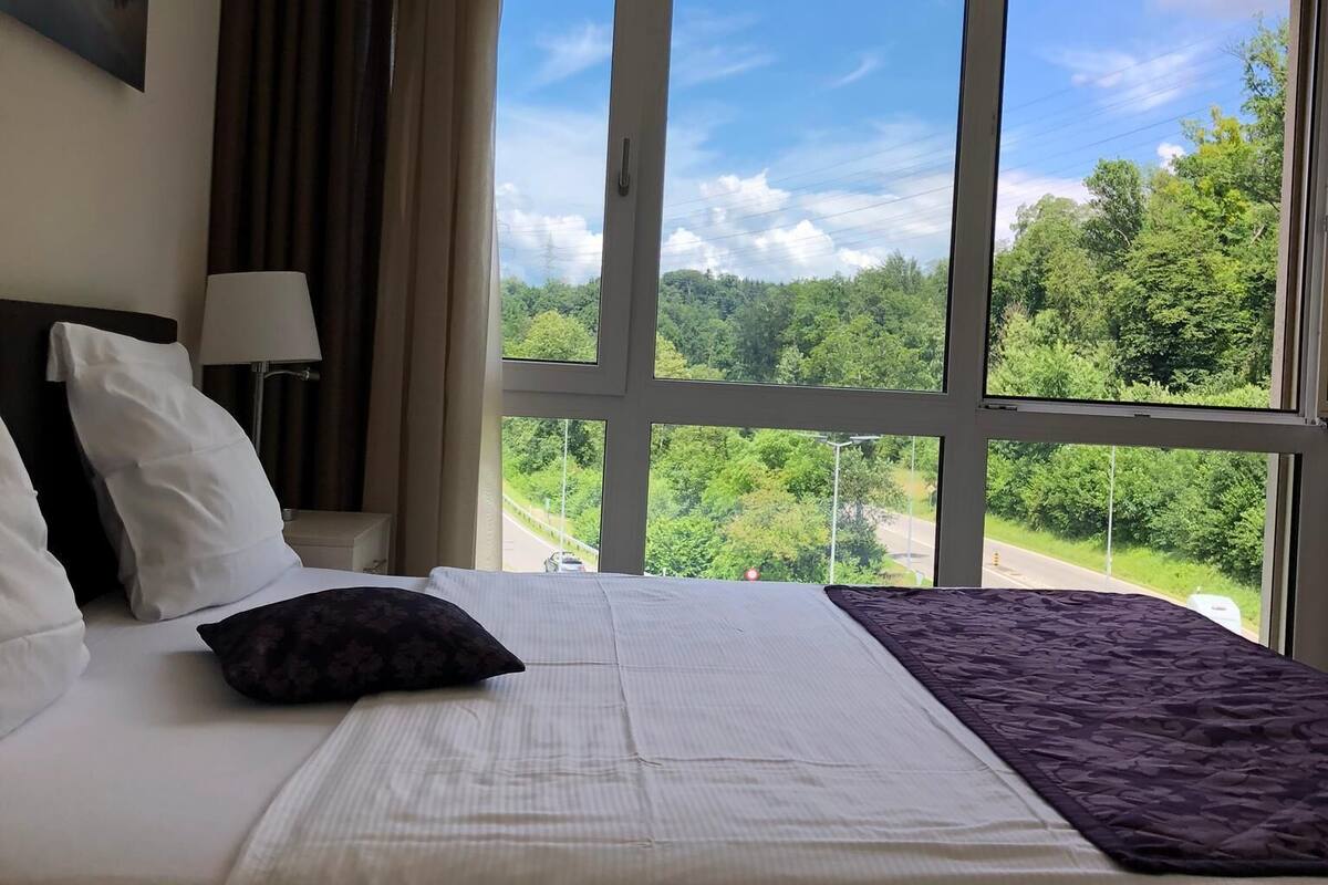 Una camera d'albergo con un letto grande, un comodino, una lampada e una finestra con vista panoramica.
