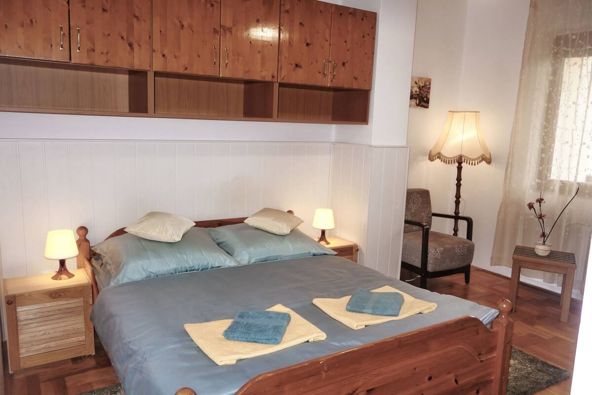 A bedroom with a wooden bed, two bedside tables with lamps, a chair, and a small table with a lamp.