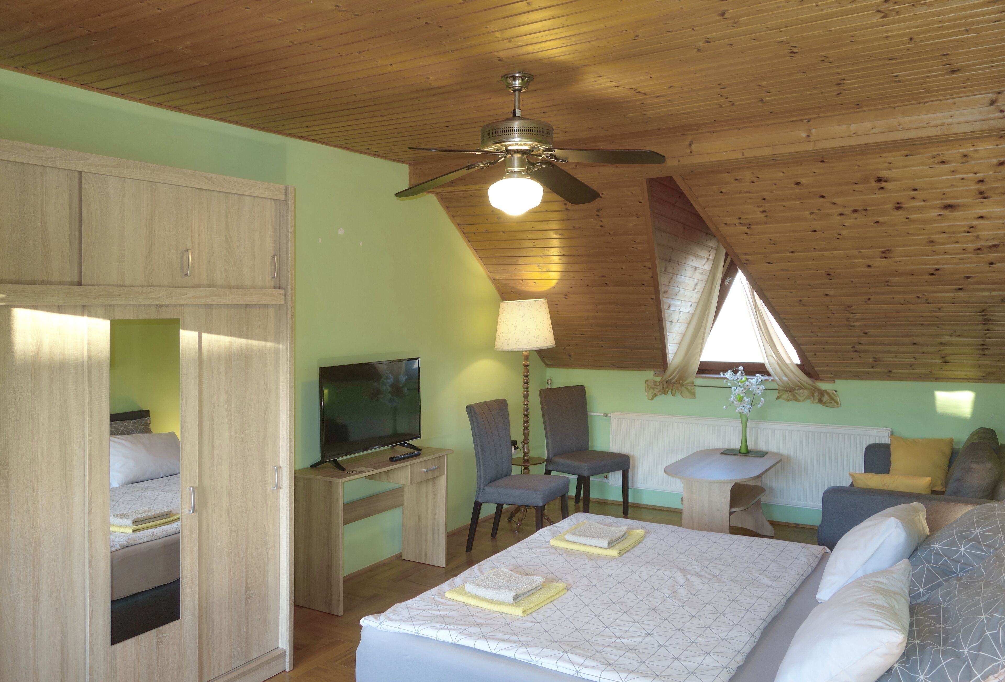 A bedroom with a bed, a desk, a chair, a TV, and a ceiling fan.