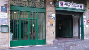 Ein Gebäudeeingang mit einem grünen Tor, einem Schild für eine Halteverbotsszone und verschiedenen Aushängen an der Wand.