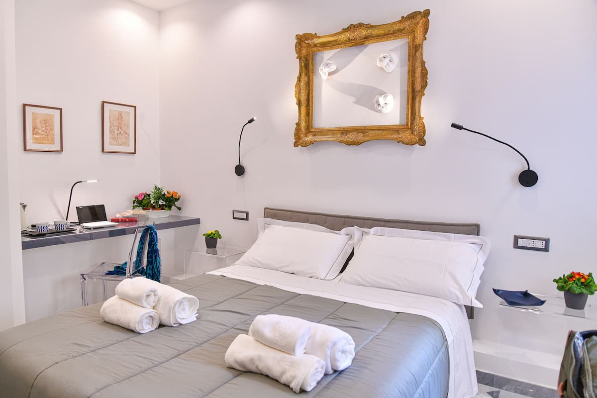 A modern hotel room with a neatly made bed, a desk with a laptop, and a large mirror on the wall.