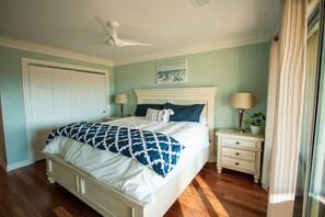 Une chambre à coucher comprenant un lit, des tables de chevet, un ventilateur de plafond, une porte et une fenêtre avec des rideaux.