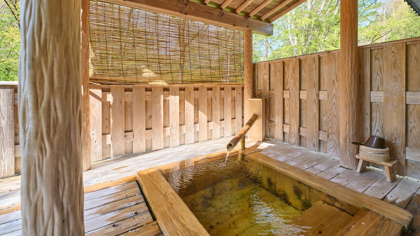 A wooden outdoor hot tub with a bamboo screen, wooden deck, and a small wooden stool.