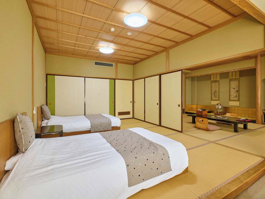 Una habitación tradicional japonesa con suelo de tatami, dos camas individuales, techo de madera y armario con puertas correderas.
