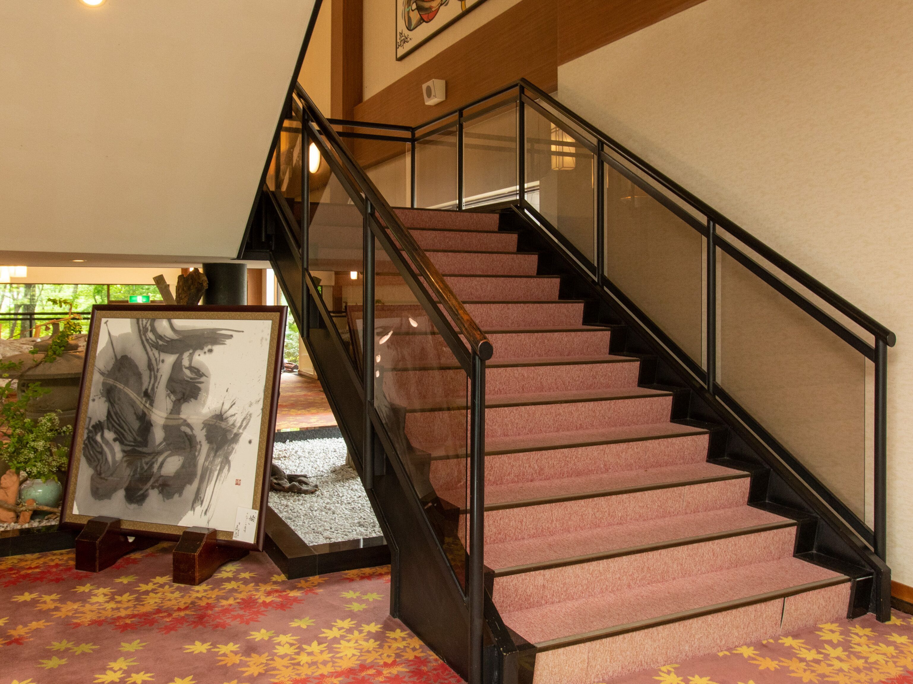 Una escalera con barandilla de vidrio, escalones alfombrados y una obra de arte enmarcada sobre el suelo.