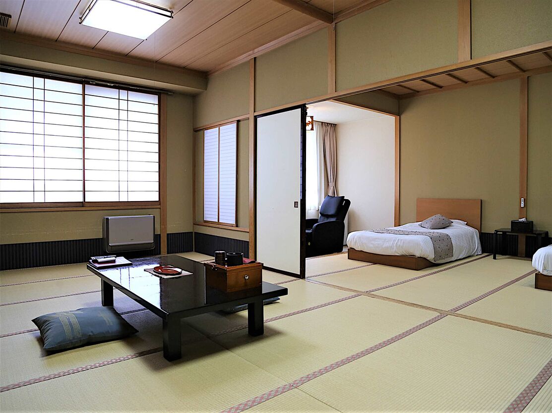A traditional Japanese room with tatami flooring, a bed, a desk with a chair, and a sliding door.