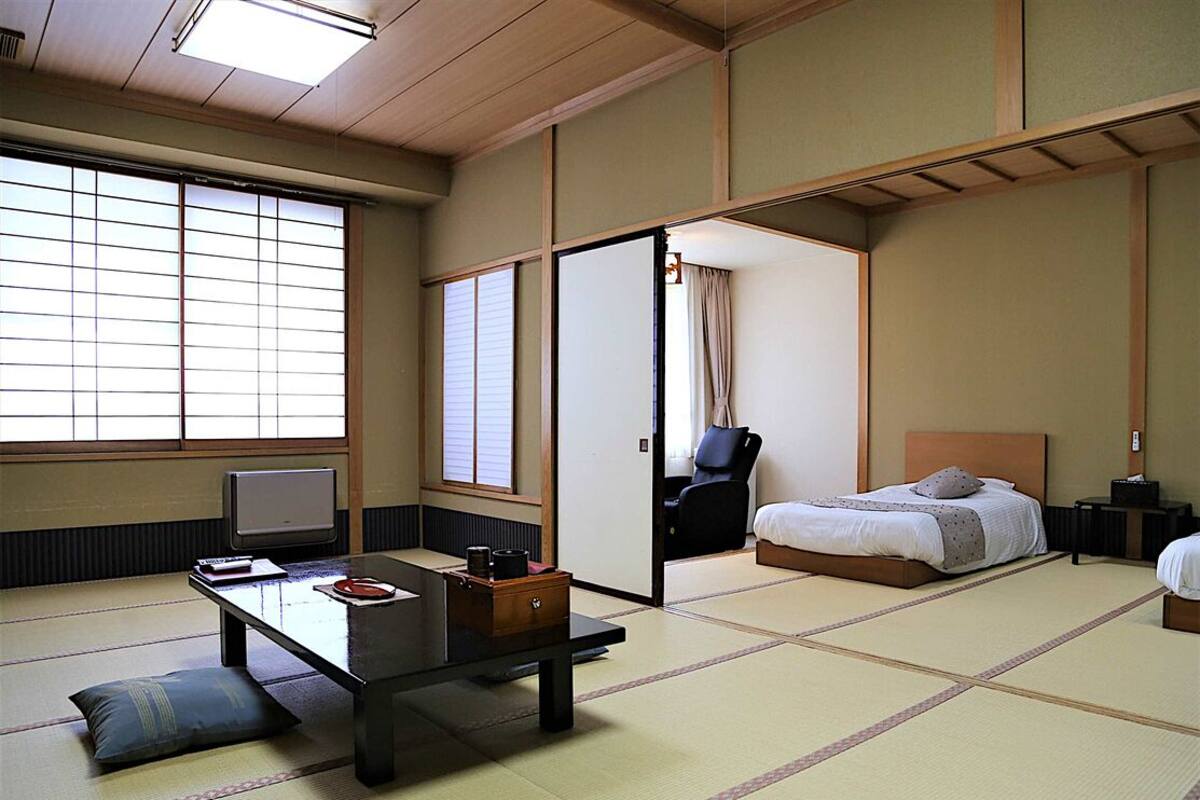 Una habitación japonesa tradicional con suelo de tatami, una cama, un escritorio con una silla y una puerta corredera.