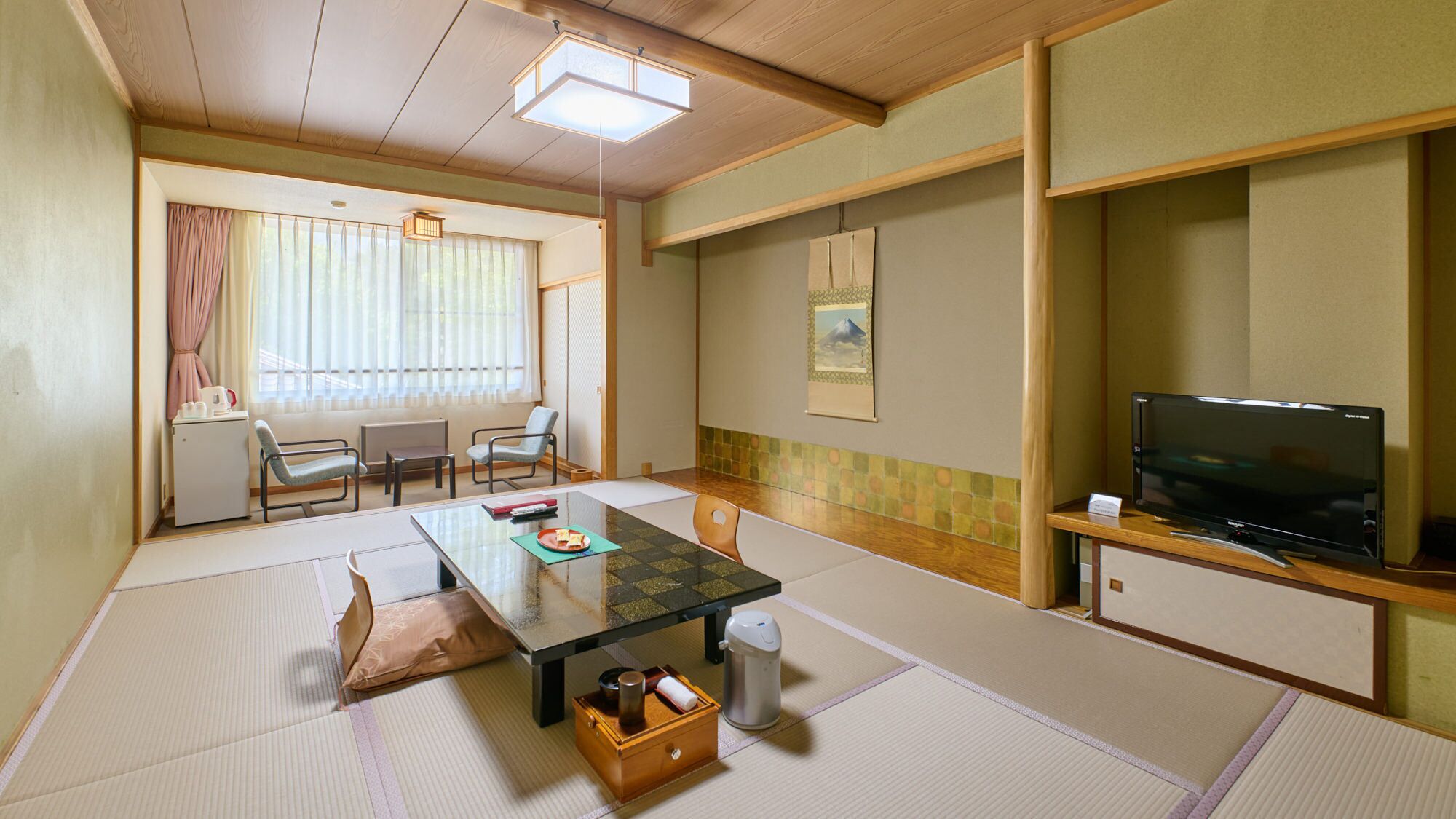 A traditional Japanese room with tatami flooring, a low table, chairs, a television, and a small refrigerator.