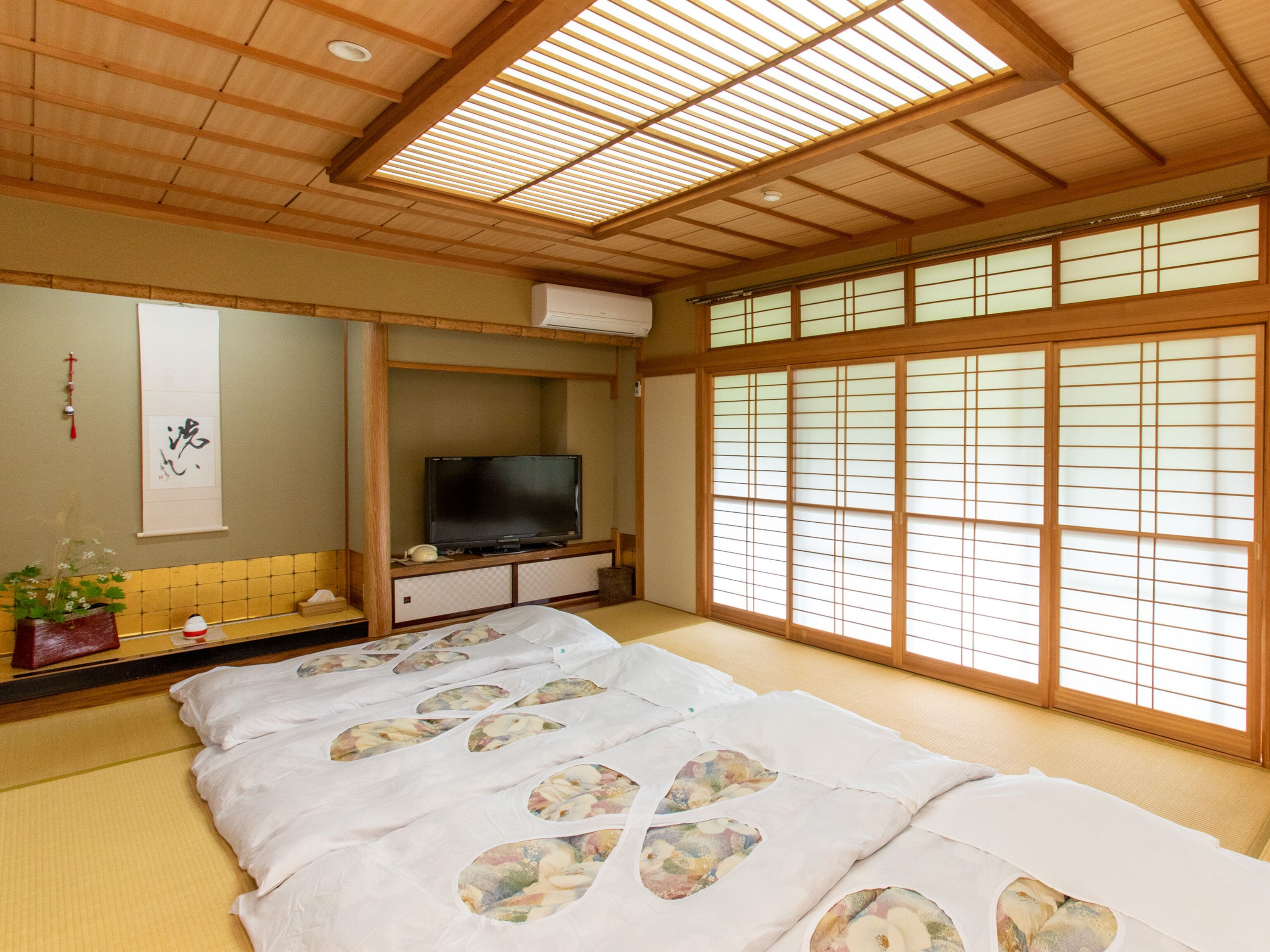 A traditional Japanese-style room with tatami flooring, a futon bed with floral patterns, a television, and sliding shoji doors.