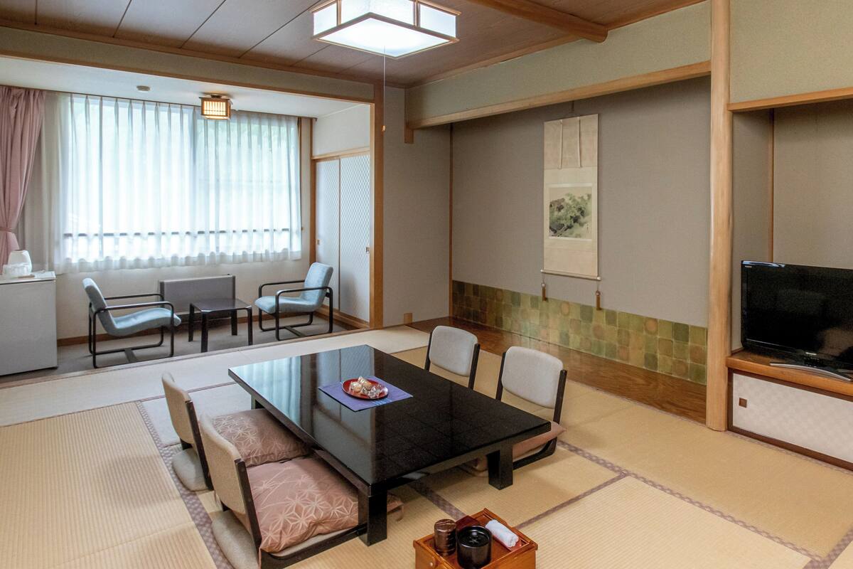 Una habitación de estilo japonés tradicional con suelo de tatami, una mesa baja con cojines, una televisión y una puerta corredera.