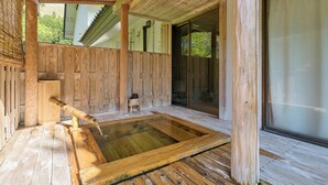 Zona de baño de aguas termales de madera con un muelle, un taburete pequeño de madera y un caño de bambú.