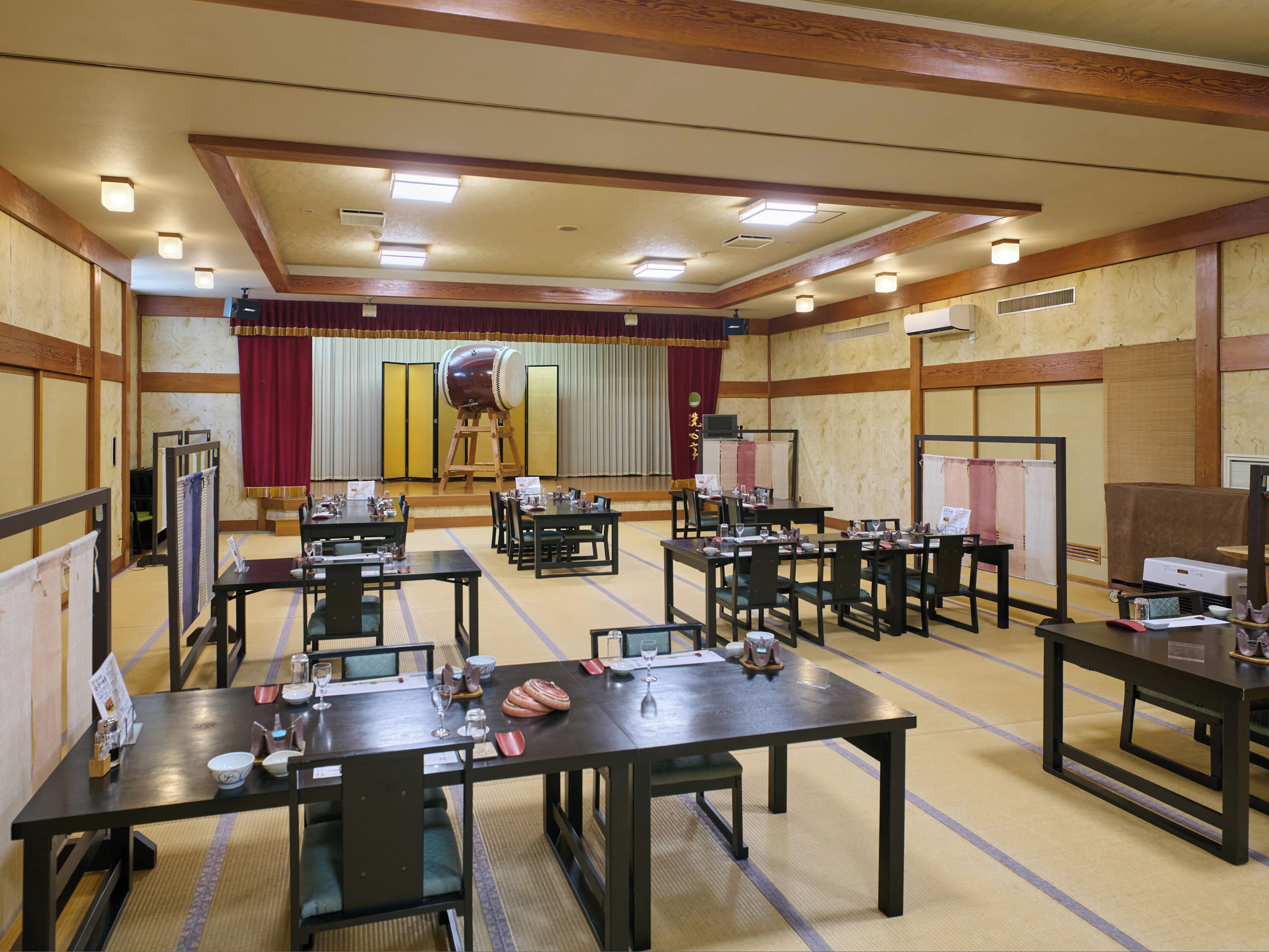 A traditional Japanese-style room with tatami mat flooring, wooden furniture, and a stage with a red curtain.