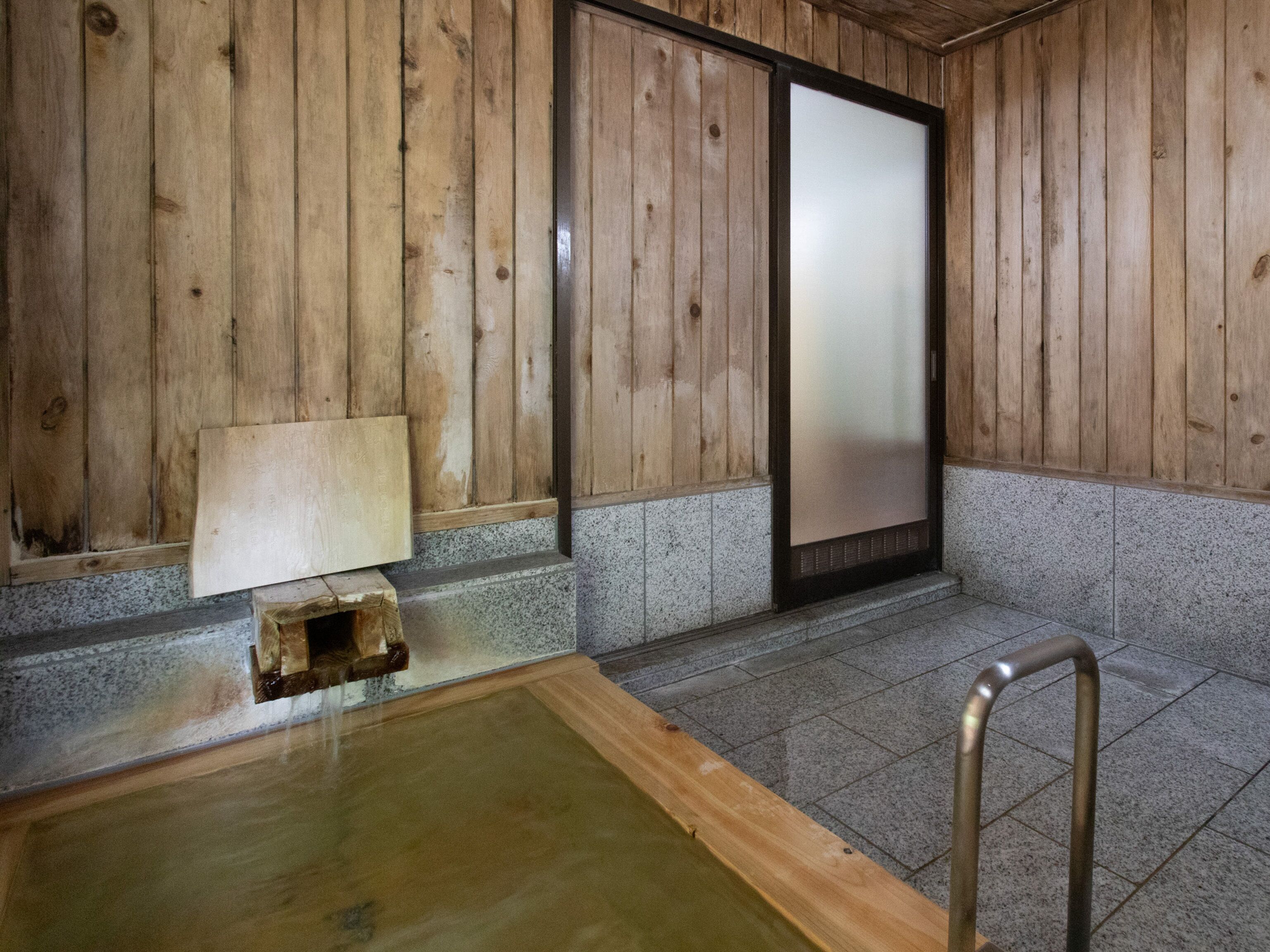 Ein traditionelles japanisches Onsen mit Holzwänden, einer Holzwanne und einem gefliesten Boden.
