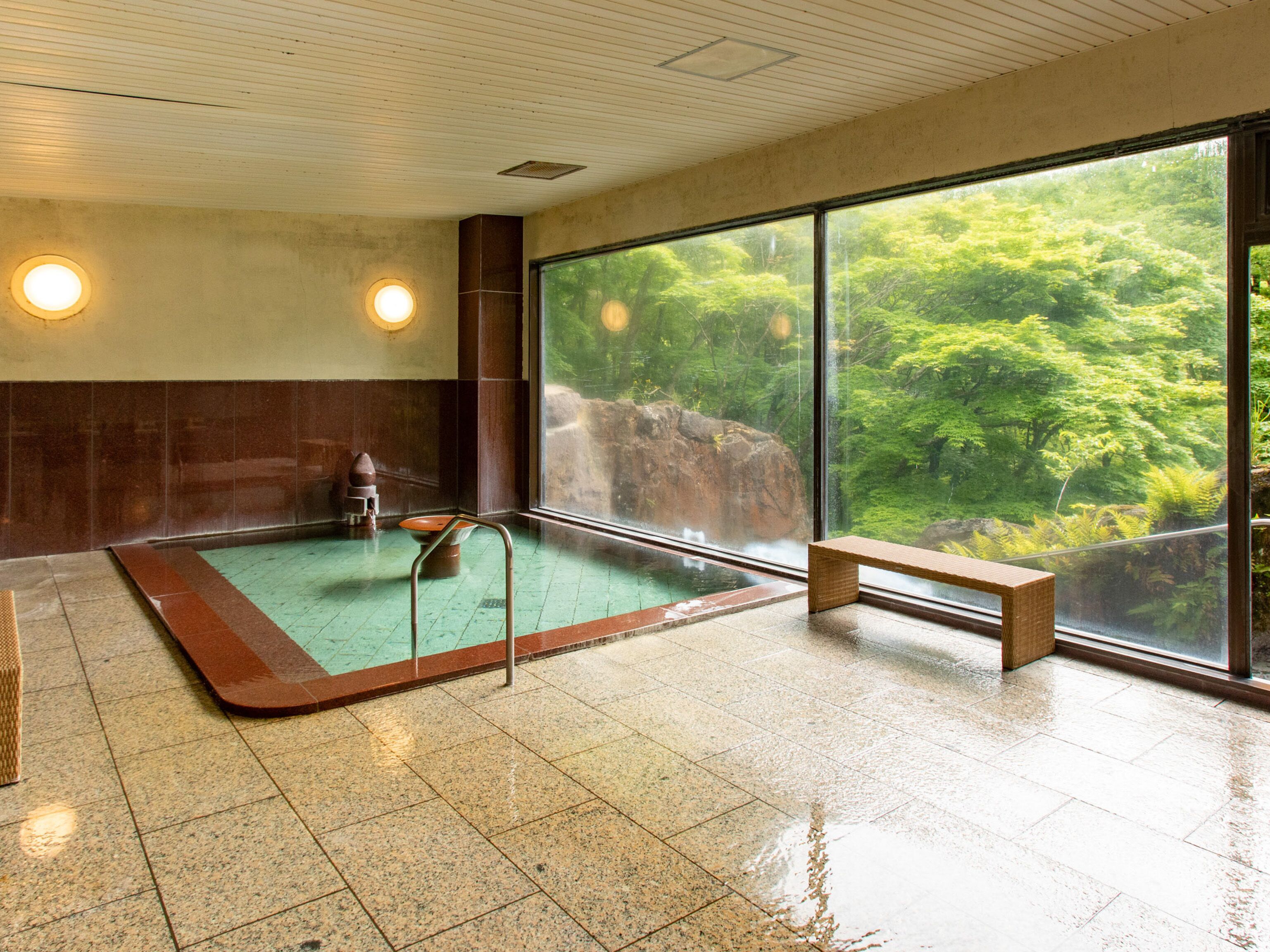Un cuarto de spa con un ventanal grande, una bañera de hidromasaje y un banco de madera.