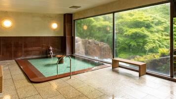 Un cuarto de spa con un ventanal grande, una bañera de hidromasaje y un banco de madera.