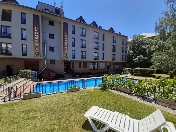 A hotel with a swimming pool, outdoor seating, and a well-maintained garden.