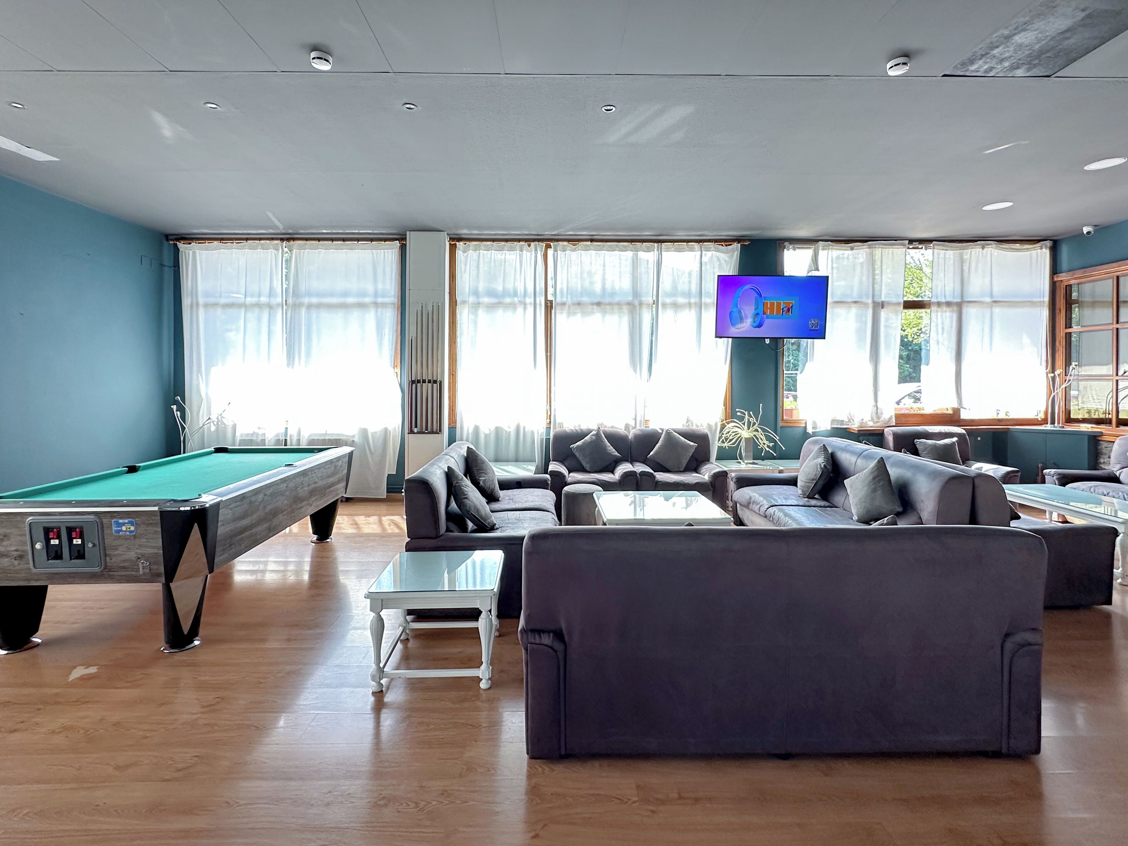 A pool table, sofas, a television, and large windows in a room.