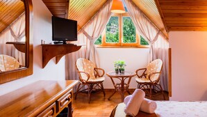 A cozy attic bedroom with a wooden ceiling, a TV on a shelf, two wicker chairs, a small table with plants, and a bed with a rolled-up towel. - Pey Resort (Sort)