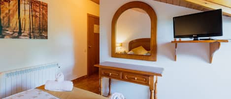 A hotel room with a bed, a wooden desk, a television, and a painting of a forest.
