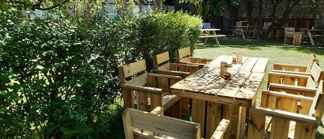An outdoor wooden deck with benches and picnic tables, surrounded by greenery and trees.