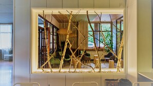 A room with a large window framed by branches, a view of an outdoor seating area, and a visible door leading to another room. - Pey Resort (Sort)