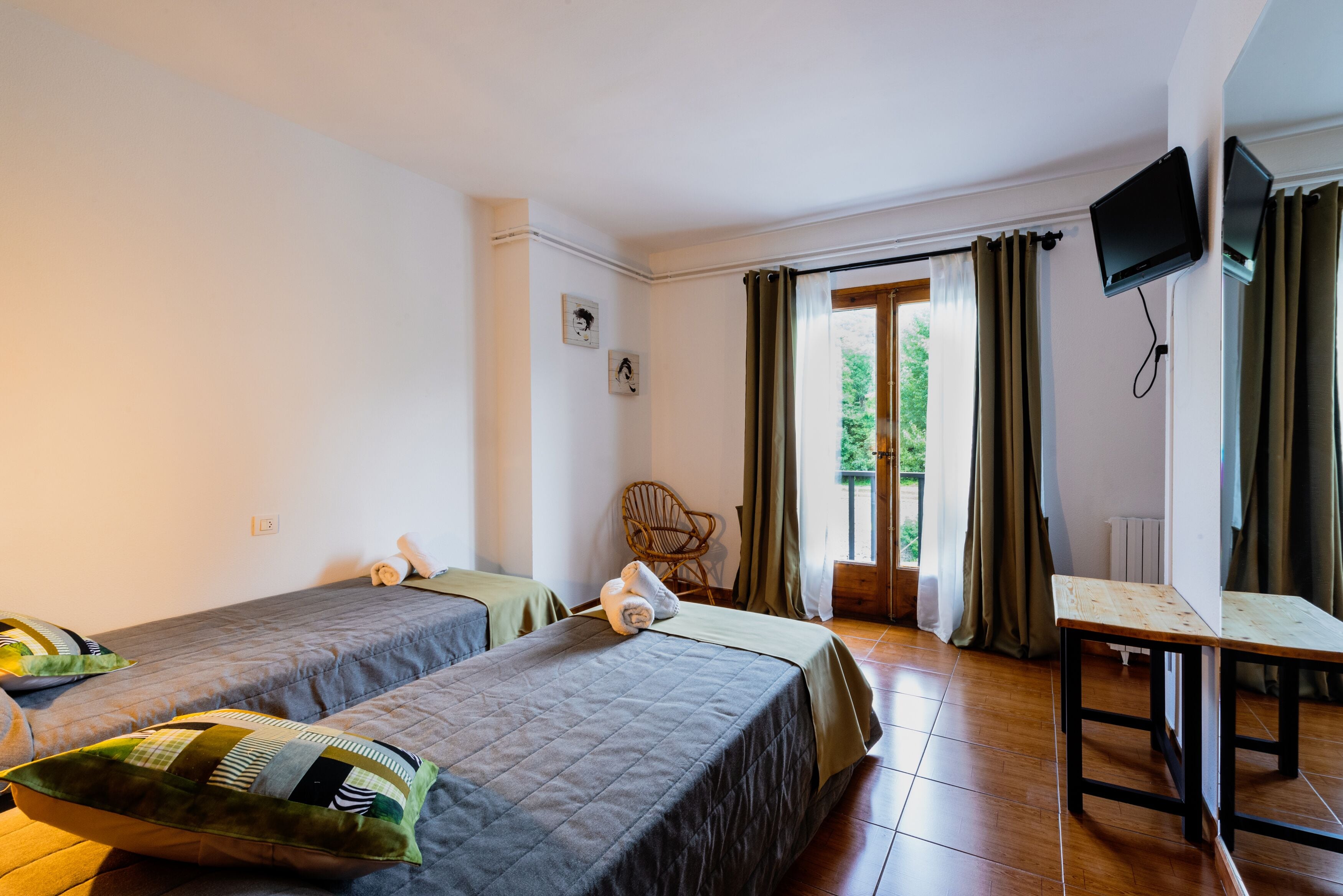 A hotel room with two beds, a chair, a table, and a TV.