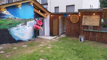 Un espacio al aire libre rústico con un mural de un río y montañas, una estructura de madera con la inscripción