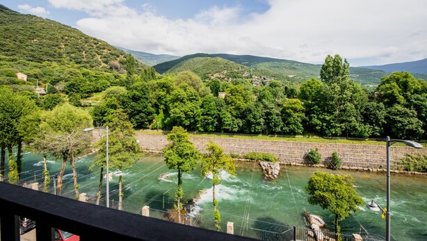 A river with a bridge, surrounded by lush greenery and hills. - Pey Resort (Sort)