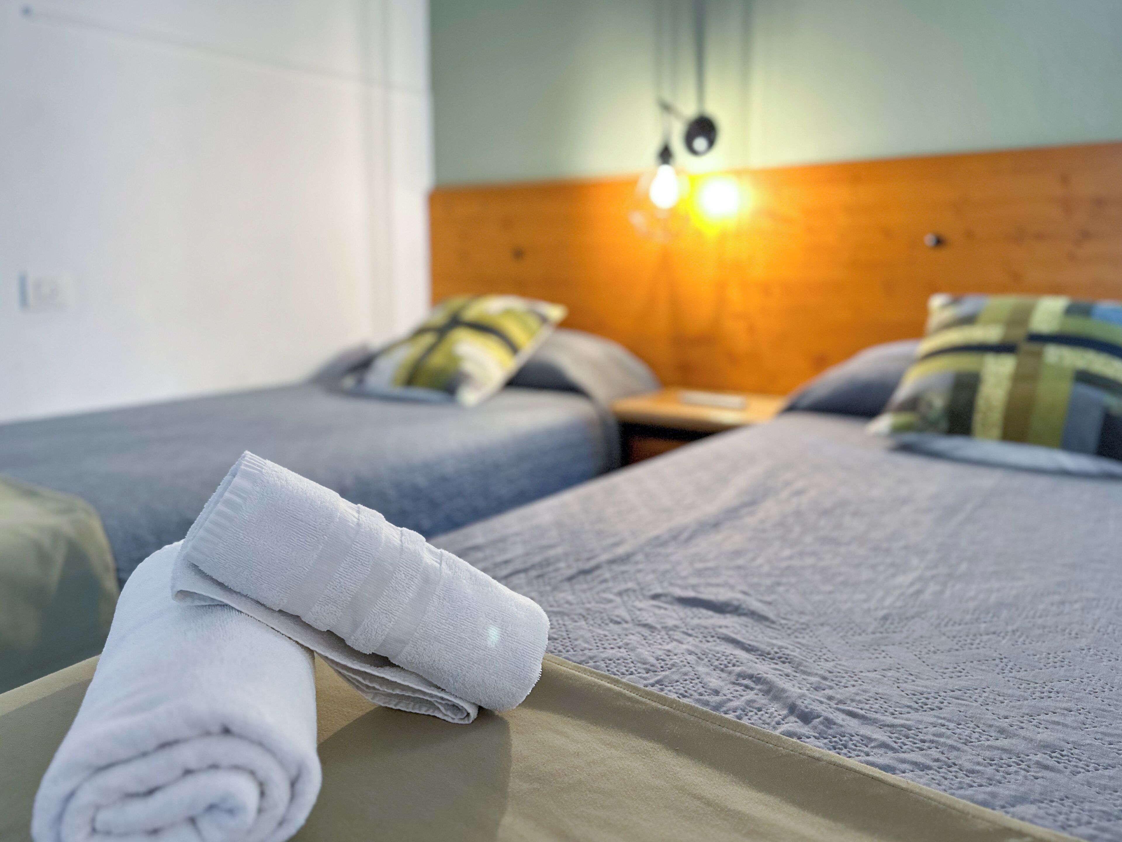 A hotel room with two beds, each with a pillow and a bedside table.