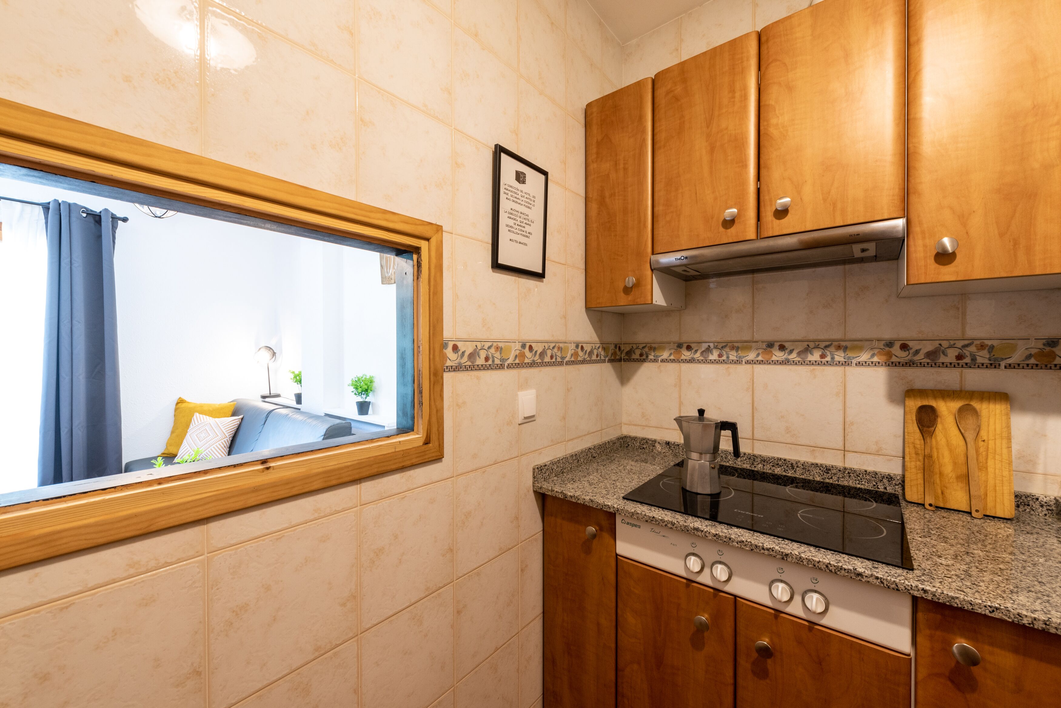 A compact kitchen with wooden cabinets, a built-in stove, and a window with curtains.