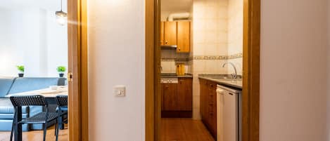 A narrow hallway leading to a kitchen with wooden cabinets and a dishwasher. A dining area with a table and chairs is visible on the left.