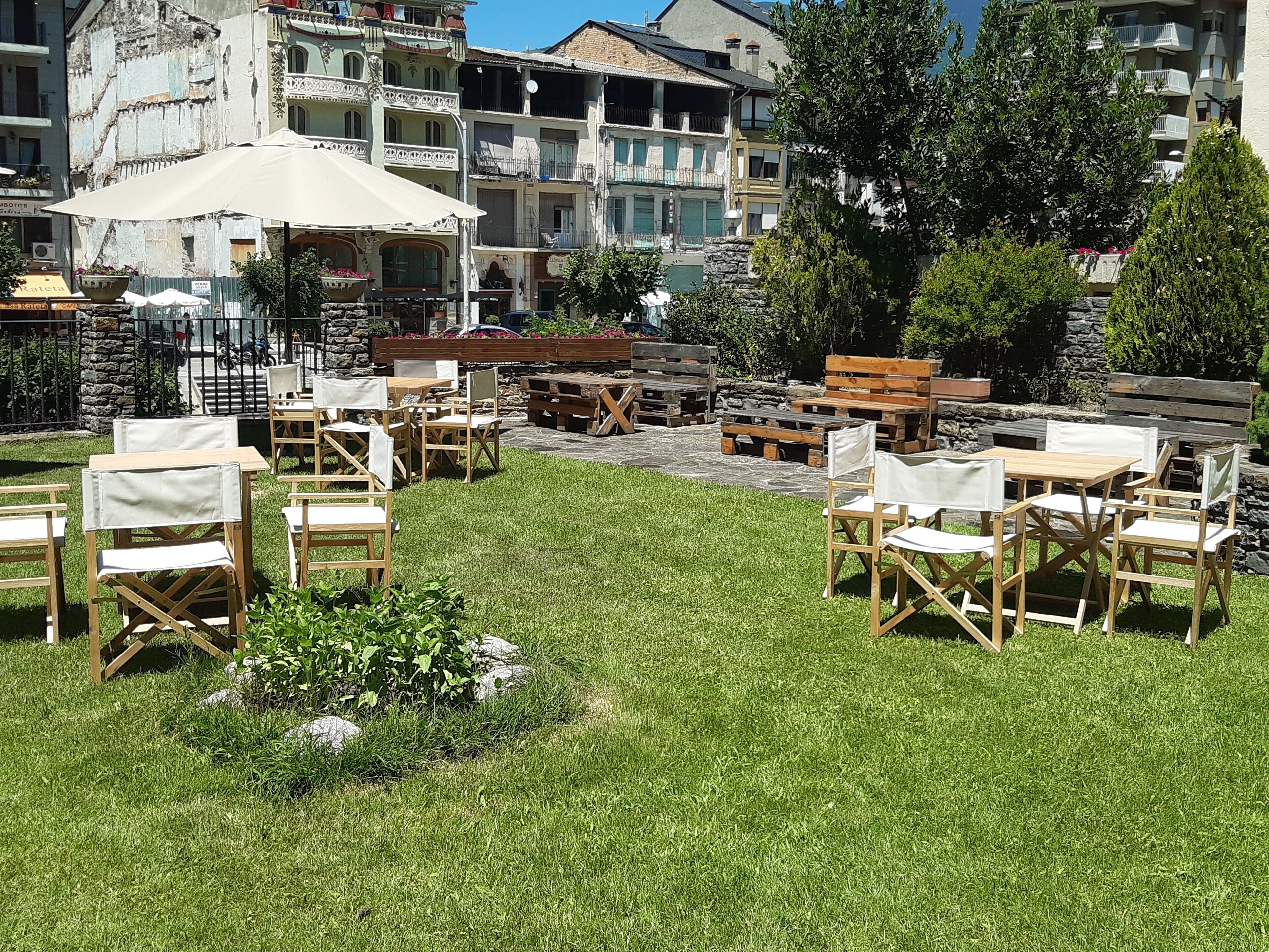 Un espace extérieur aménagé avec des tables et des chaises en bois, entouré d’une pelouse bien entretenue et de murs en pierre.