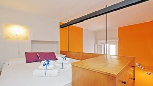 A hotel room with a bed, a wooden side table, and a wall-mounted light fixture.