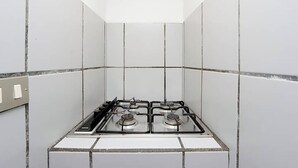 A kitchen with white tiled walls, a gas stove, and a light switch on the left.