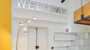 A modern interior with a 'WELCOME' sign, a floor lamp, and white tiled walls.