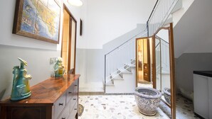 A hallway with a wooden floor, a tiled wall with a map, a staircase, and a large window.