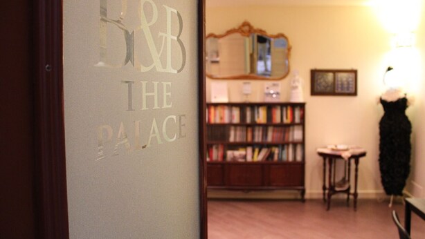 A room with a bookshelf, a mirror, and a black dress on a chair.