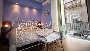 A bedroom with a metal bed frame, a bedside table with a lamp, and a view of a balcony with outdoor furniture.