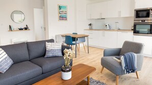 A modern living room with a grey sofa, a wooden coffee table with a vase, a blue armchair, and a dining area with a wooden table and chairs. - Port Ste-Marine: L'Escale - Balconies & Small view (Combrit)
