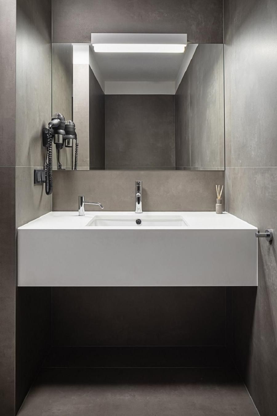 A modern bathroom with a large mirror, a white sink, and a built-in telephone.