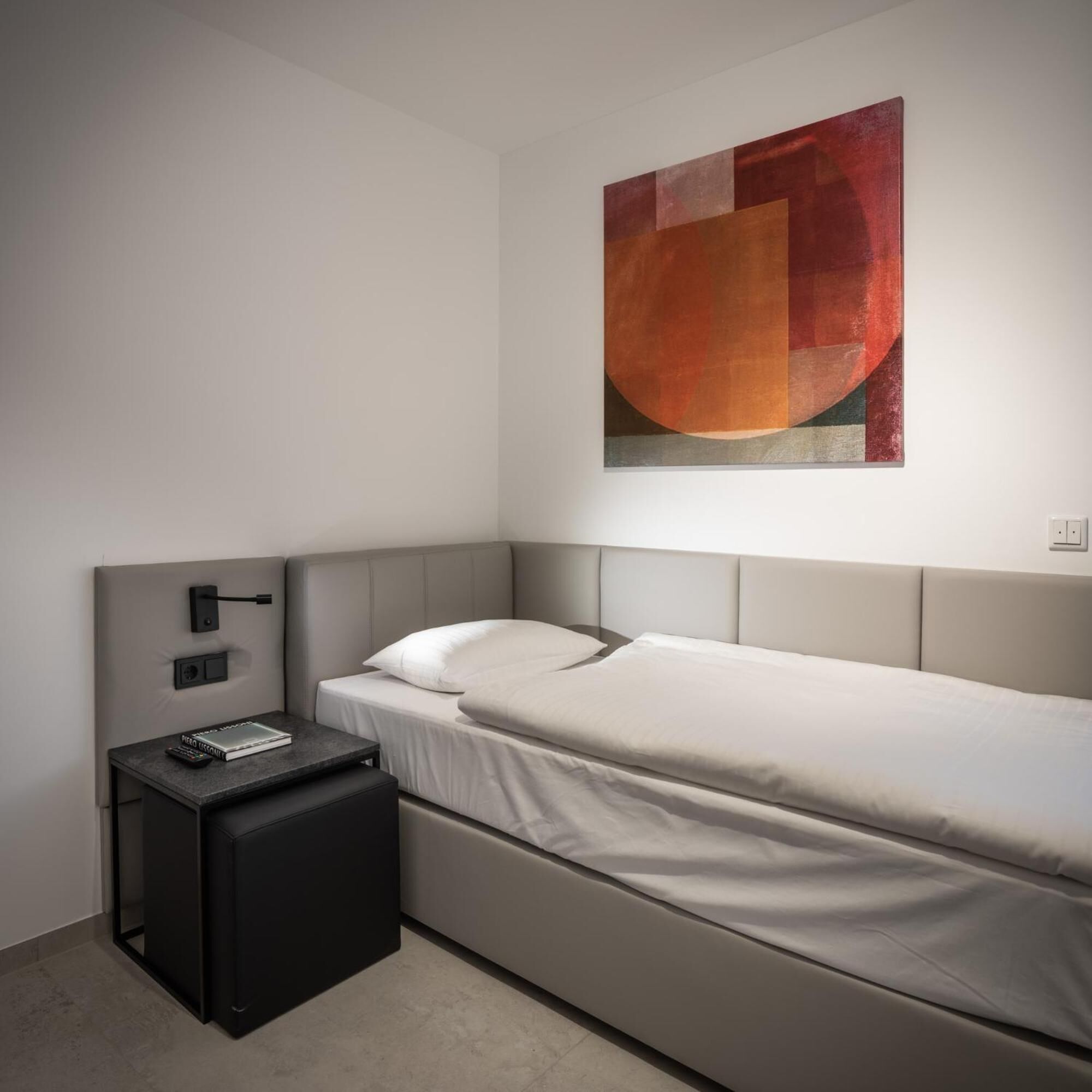 A modern bedroom with a single bed, a bedside table, and a wall-mounted artwork.