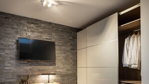Une chambre moderne avec un mur en pierre, un téléviseur à écran plat, un bureau avec une chaise et un dressing avec des portes coulissantes.