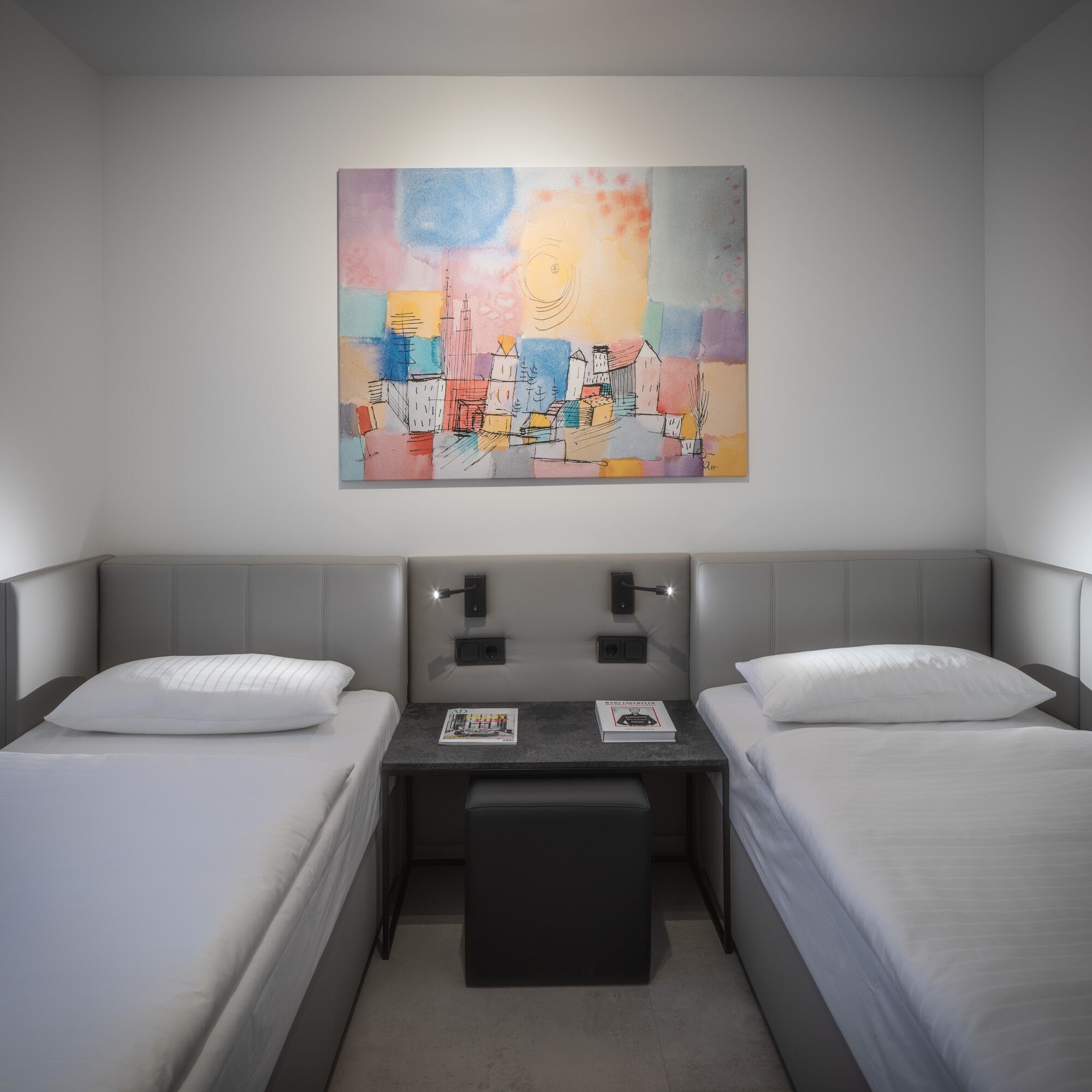 A hotel room with two beds, a small table, and a colorful abstract painting on the wall.