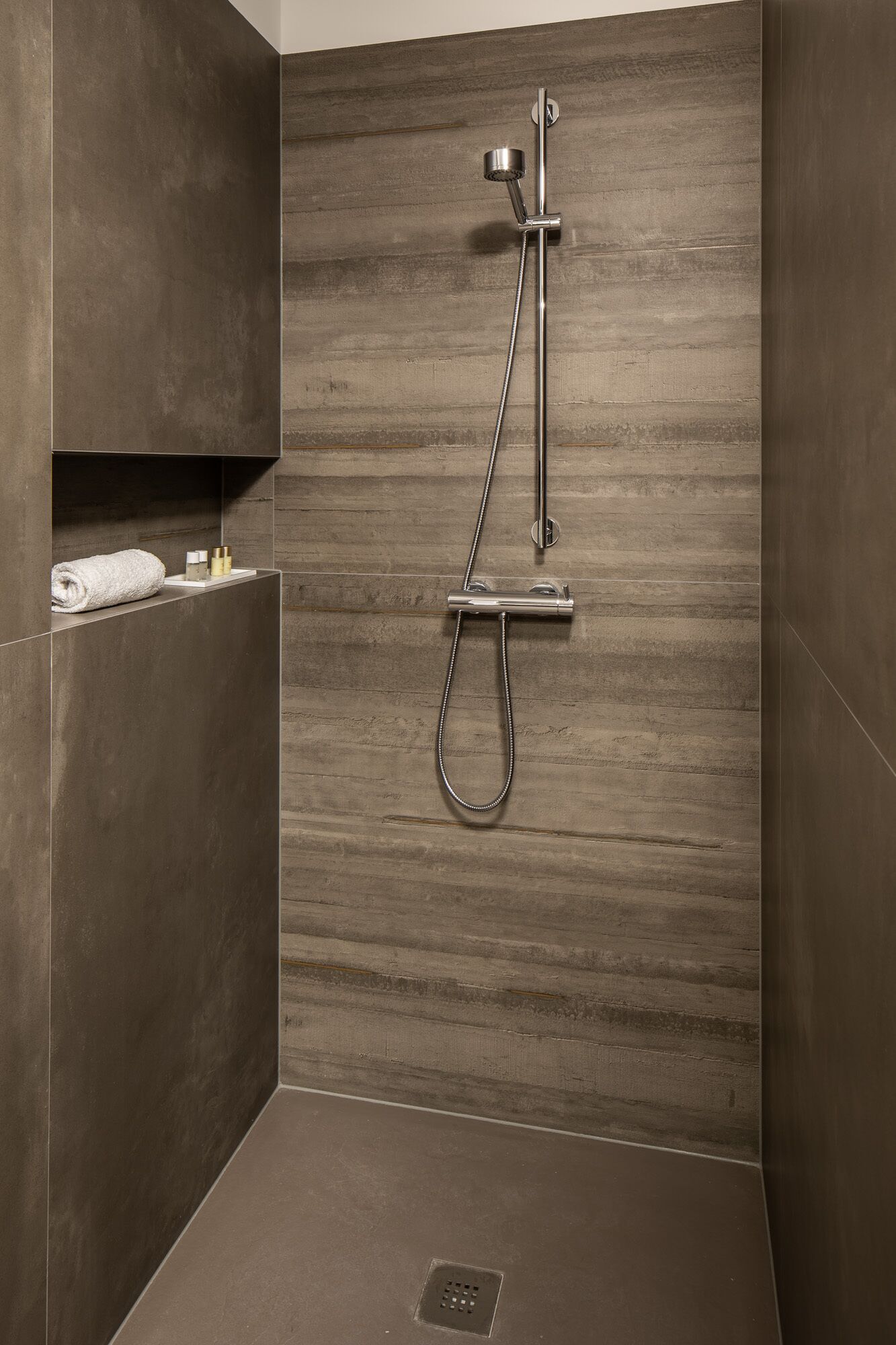 Una ducha moderna con pared de paneles de madera, cabezal de ducha de mano y panel de control.