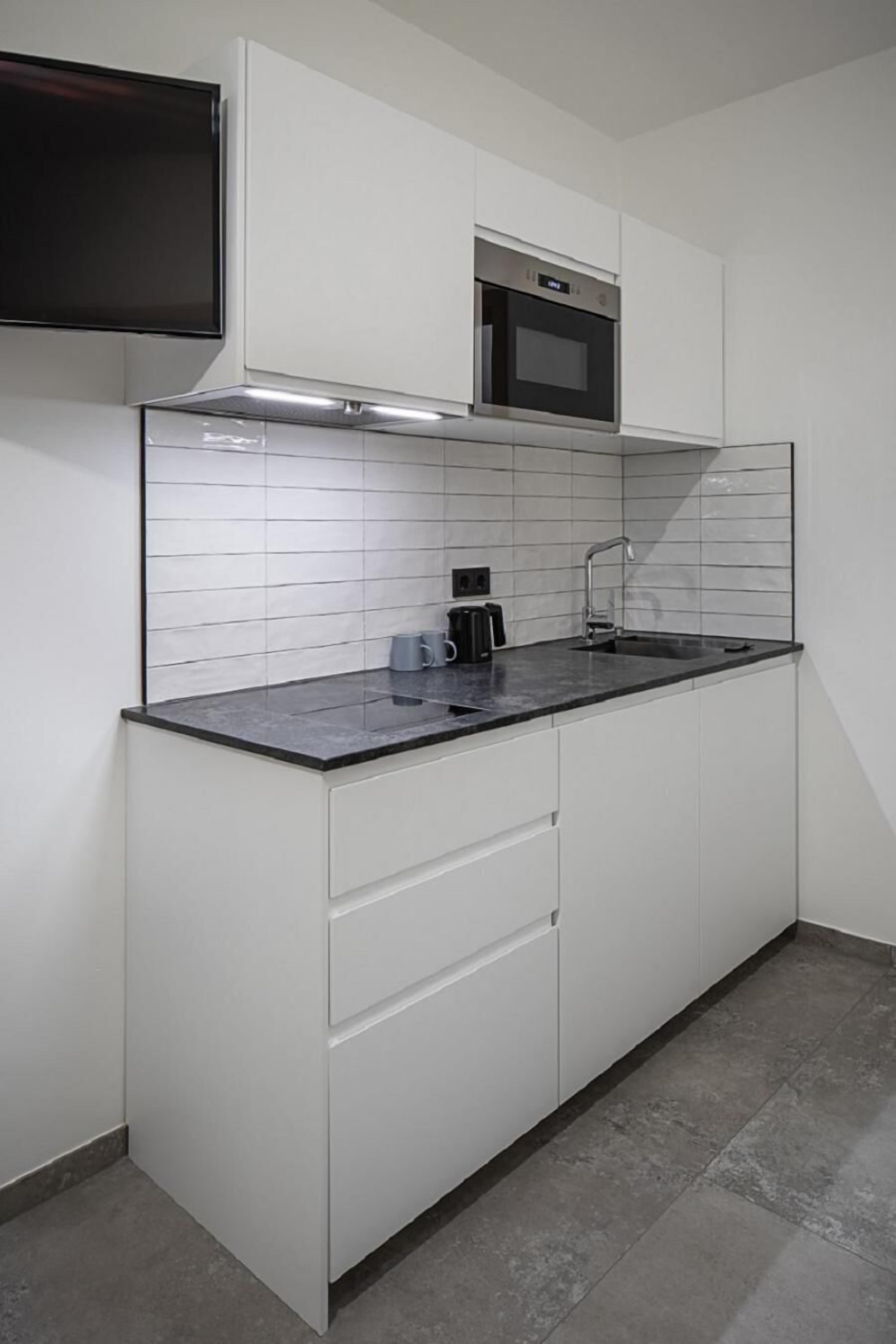A modern kitchen with white cabinetry, a black countertop, a microwave, and a built-in oven.