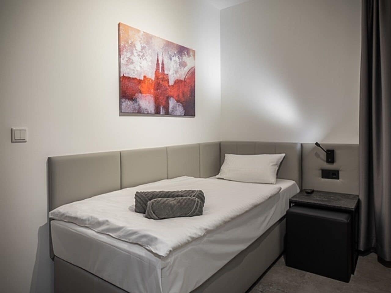 En pænt redt seng med pude, et sengebord med lampe, og et billede på væggen.