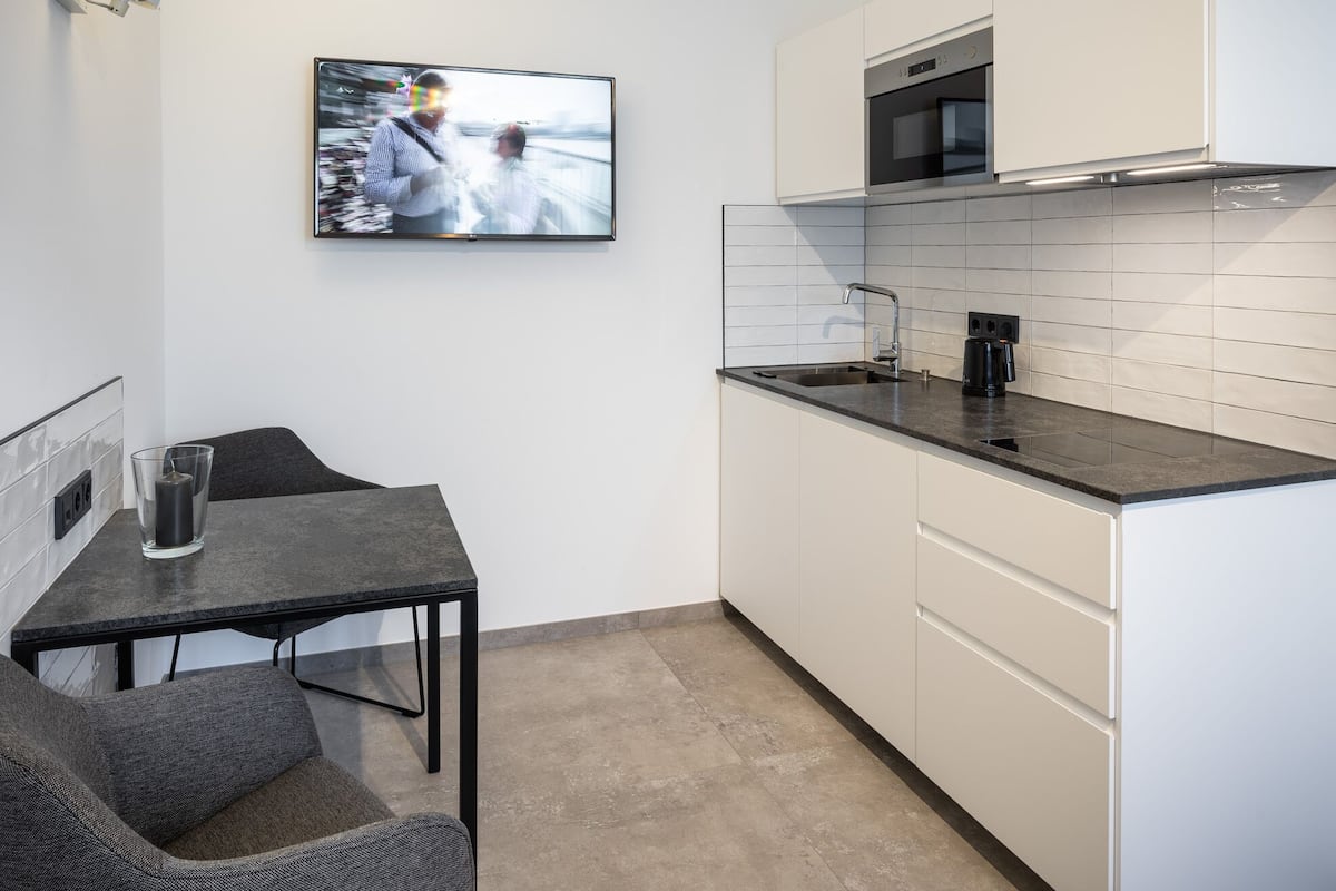A modern kitchen with white cabinets, a black countertop, and a built-in oven. There's a glass table with a candle and a chair.