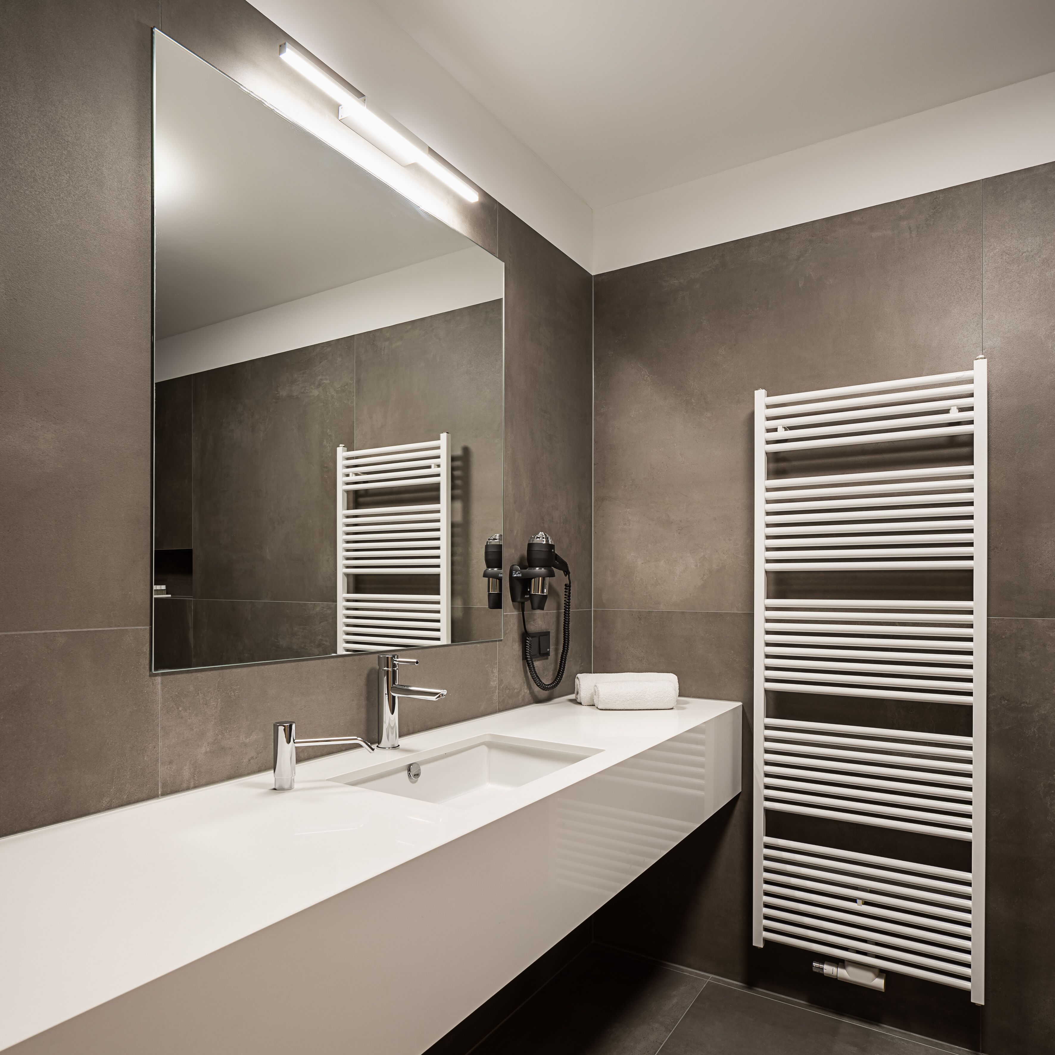 Une salle de bain moderne avec un lavabo blanc, un grand miroir et un sèche-serviettes.
